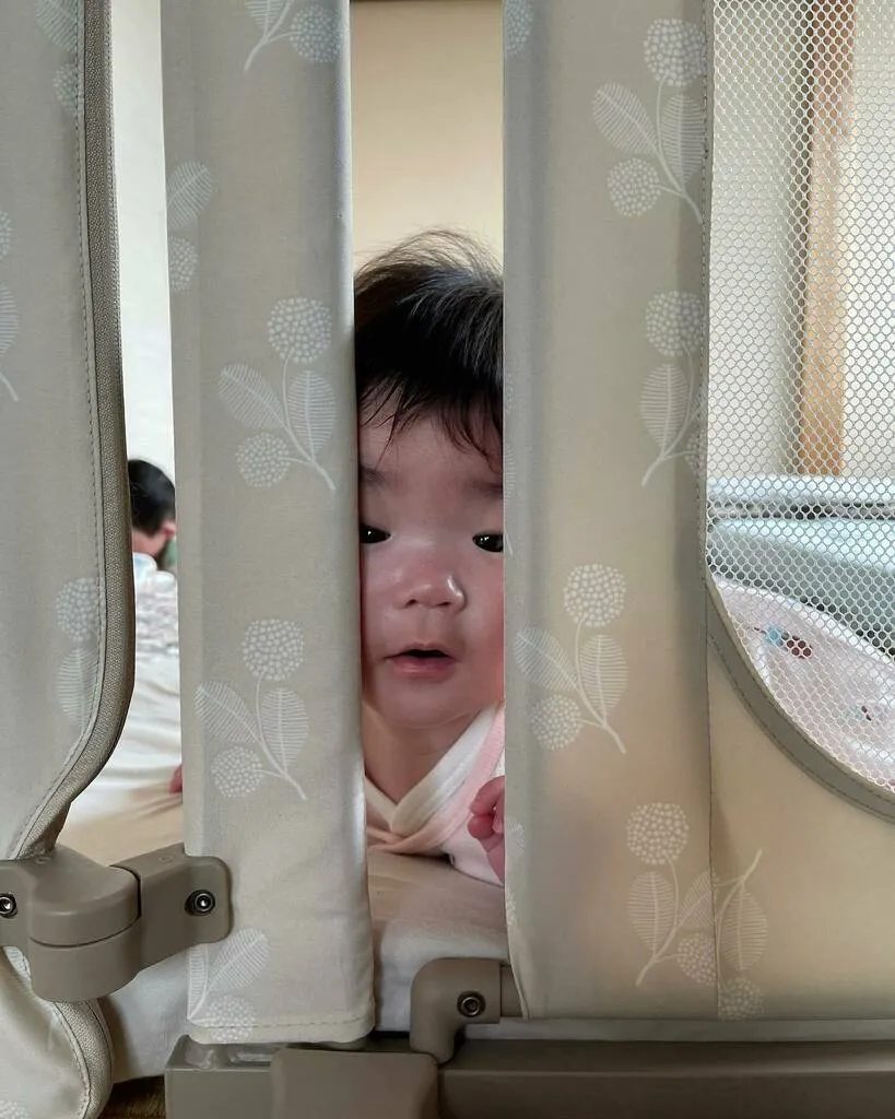 ベビーゲートのカーテンの隙間から顔を出す子ども