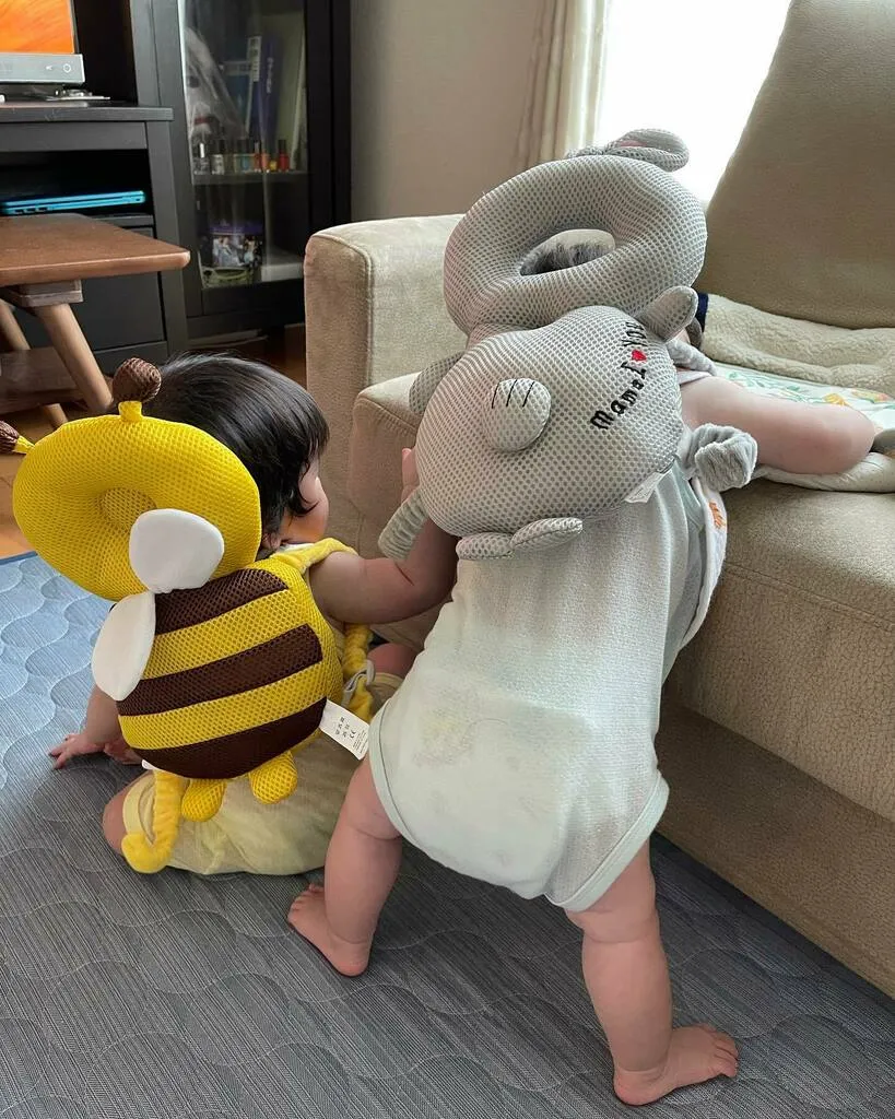 背負うタイプのクッションを着けてソファにつかまり立ちする2人