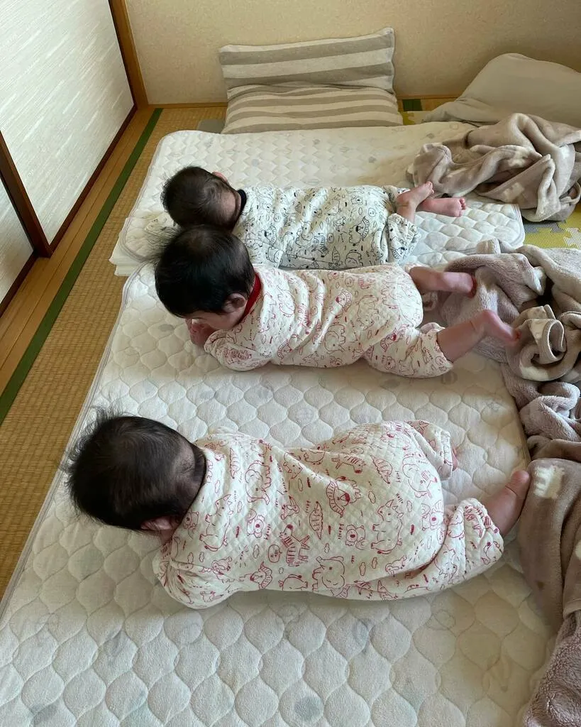 布団の上で3人並んでうつ伏せの練習をする三つ子